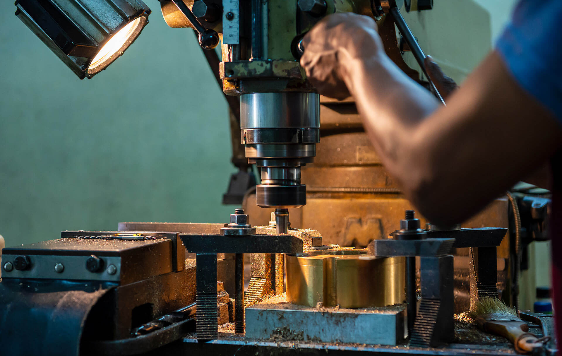 Person using a manual mill while a spotlight illuminates workspace