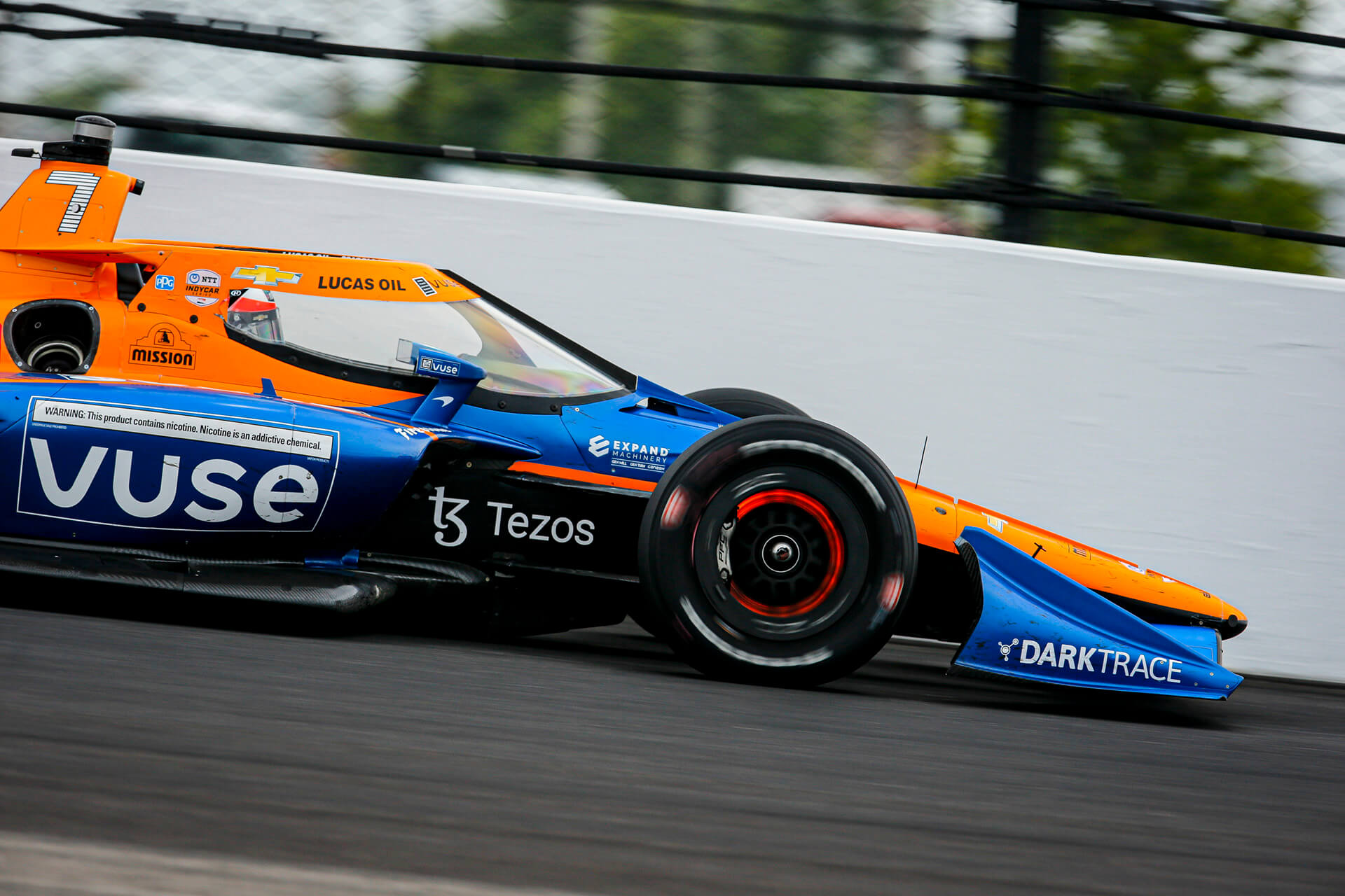 Fast motion capture of an orange and blue racecar with the Expand Machinery logo visible behind the front wheel